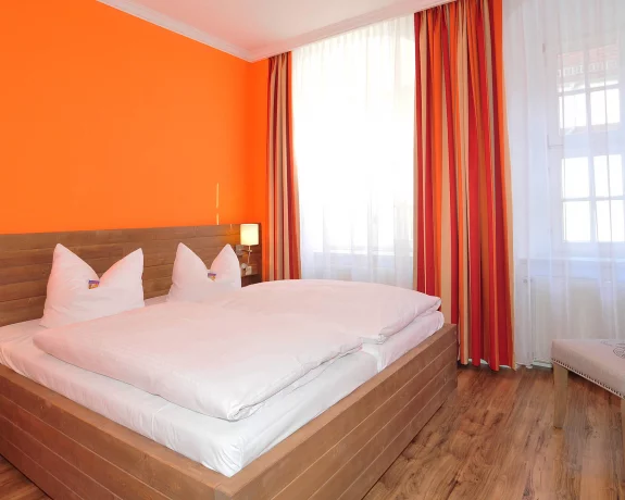 Bühnenbild: Hotelzimmer in Freiberg mit orangenen Wänden und einem Doppelbett